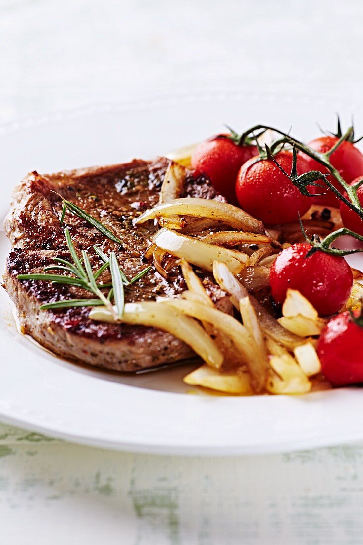 Gegrilltes Schweinesteak mit gebratenen Zwiebeln und Kirschtomaten