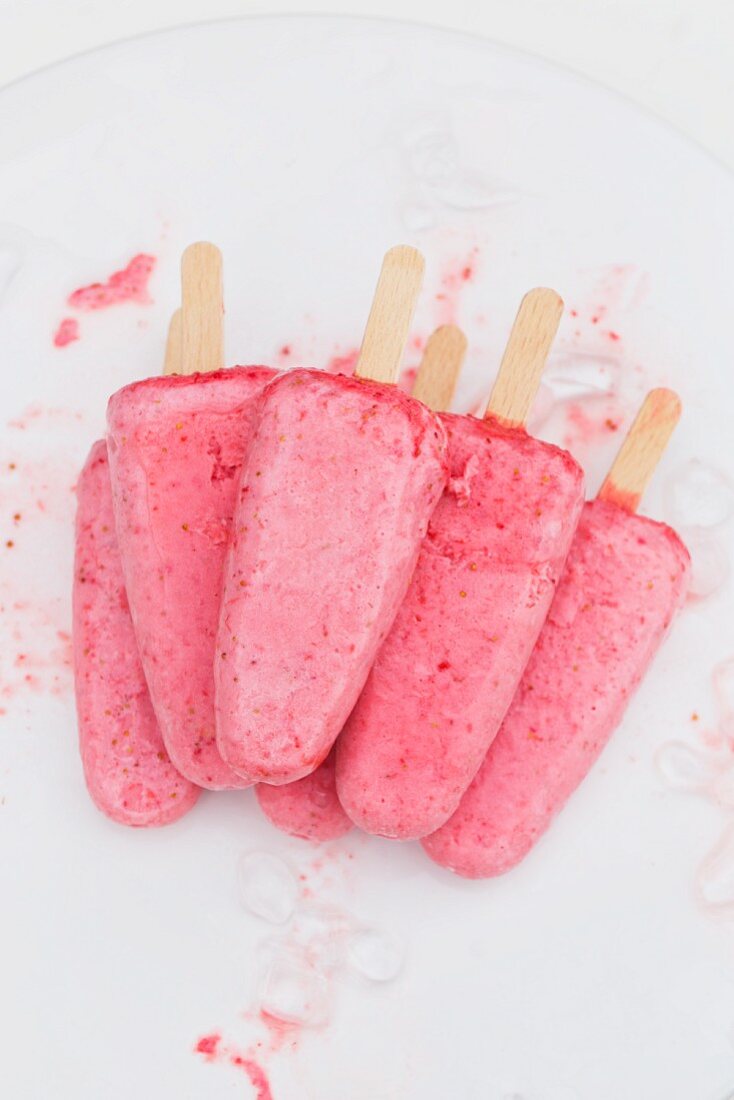 Strawberry ice cream sticks on a cake plate with bits of crushed ice