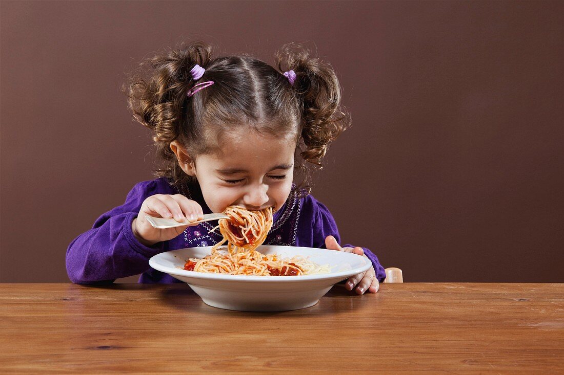 A little girl eating spaghetti with her eyes closed