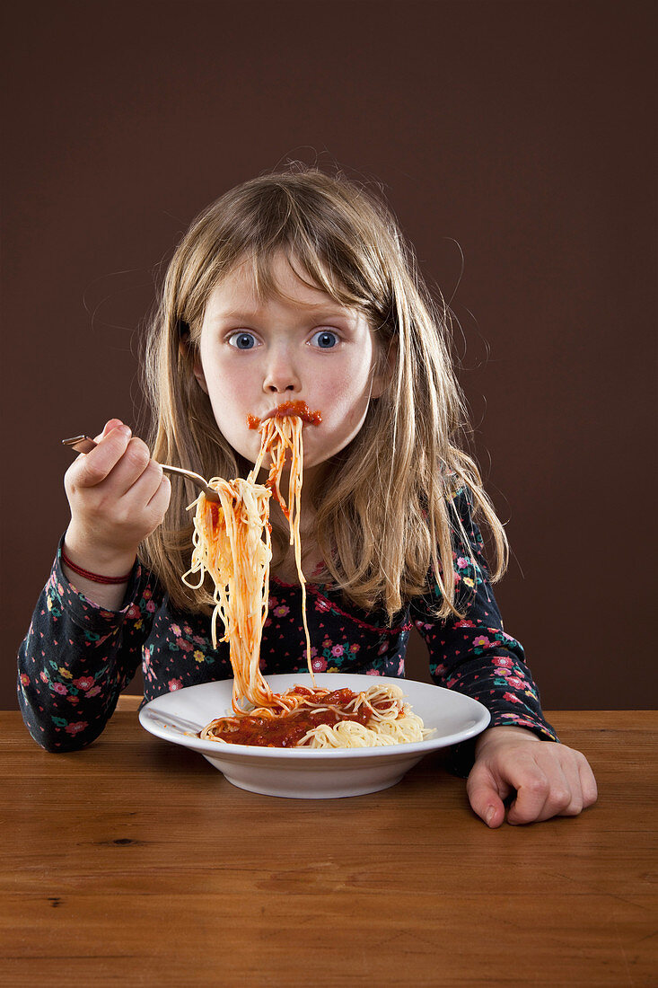 A little girl smeared with tomato sauce eating spaghetti