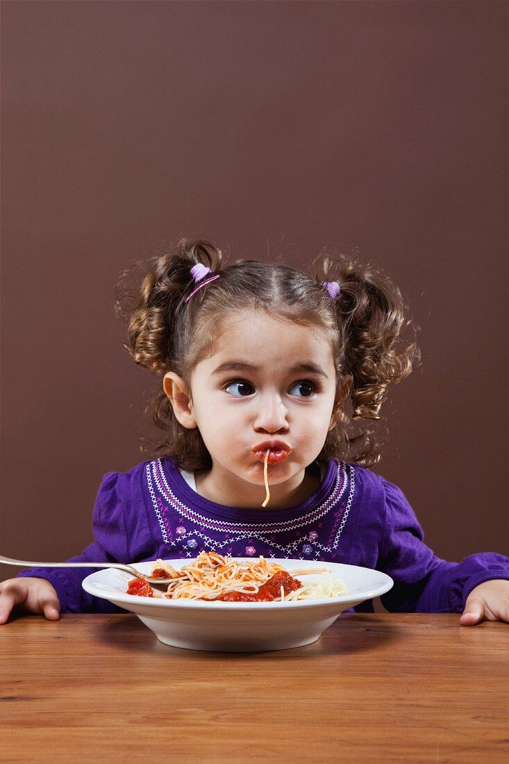 A little girl eating spaghetti sucking a strand into her mouth