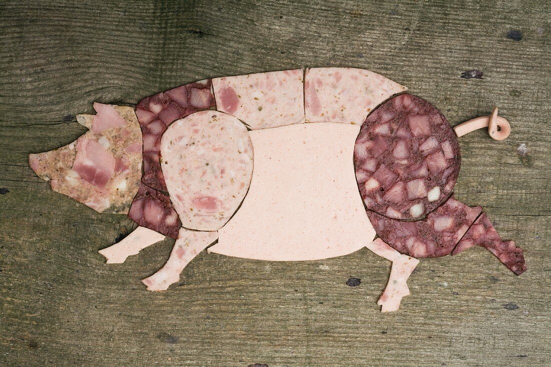 Cold cuts of meat arranged in the shape of a pig on a wooden surface
