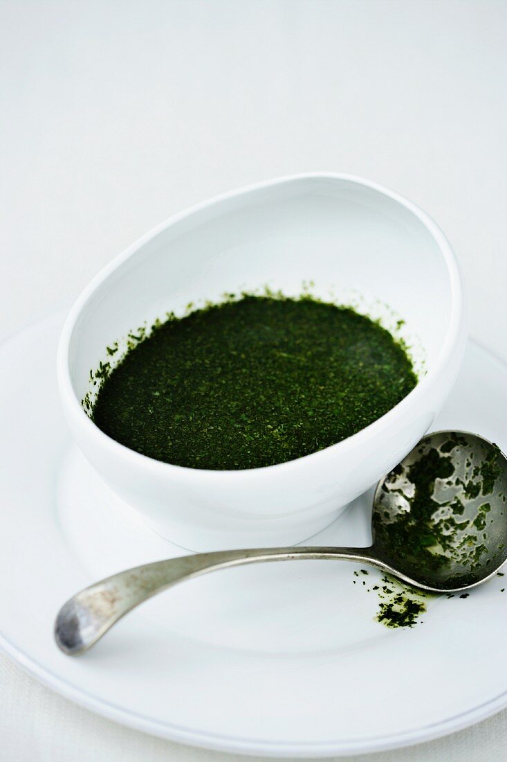 A bowl of mint sauce next to a sauce ladle