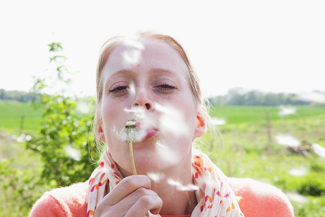 Junge Frau bläst auf eine Pusteblume