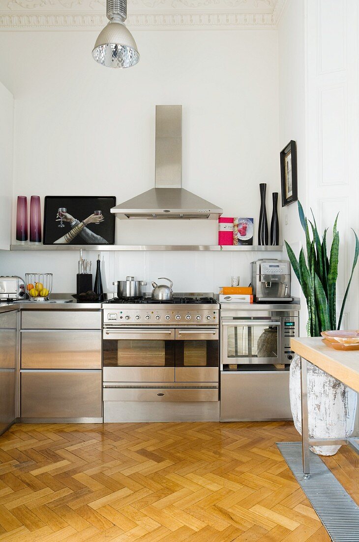 Stainless steel fitted kitchen with extractor hood, floating shelf and pristine, oak herringbone parquet floor