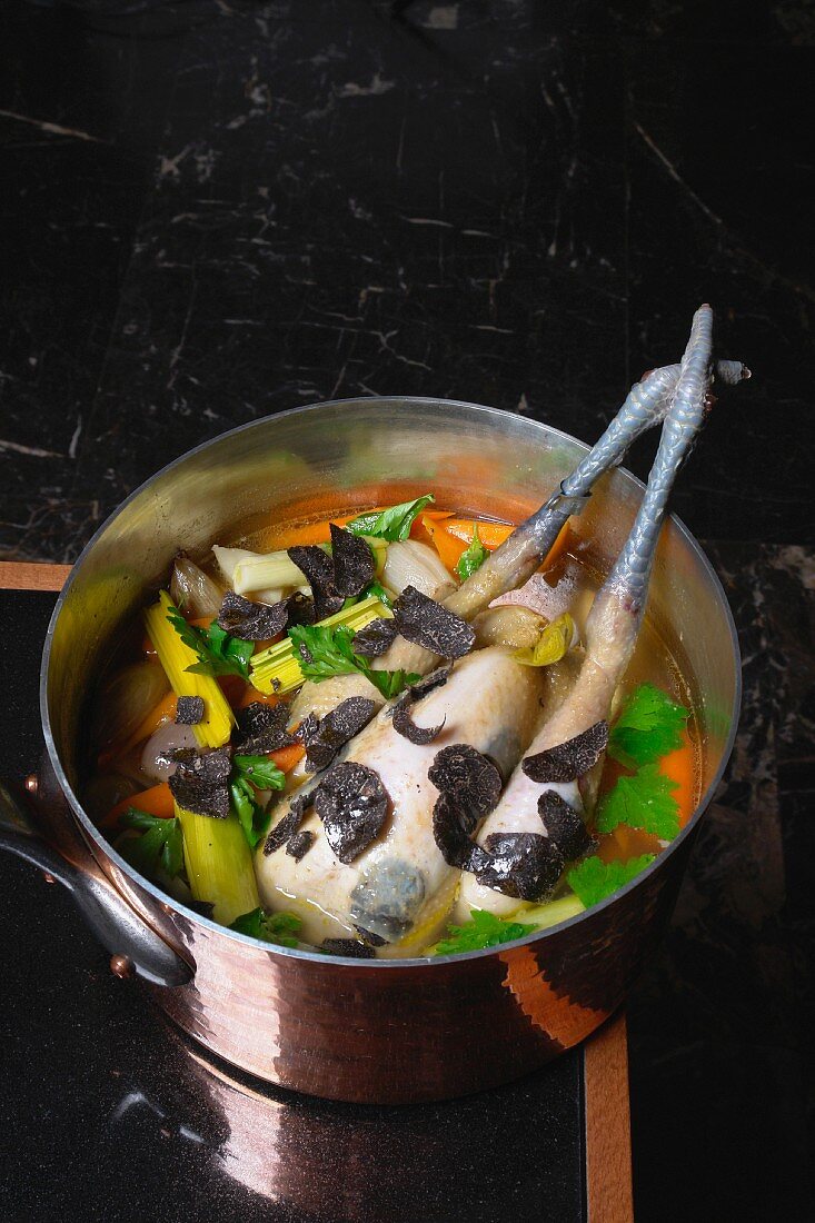 Chicken soup with a whole chicken, black truffles and vegetables in a copper pot