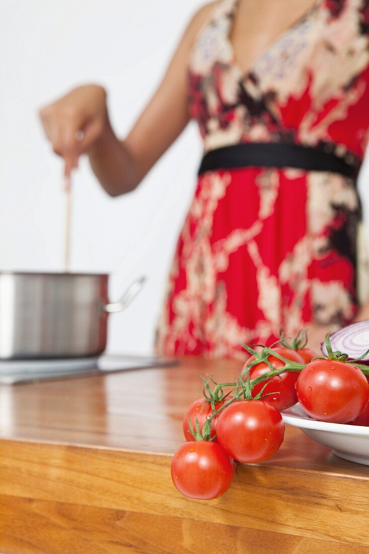 Vine tomatoes on a work surface with a woman in the background stirring a pot