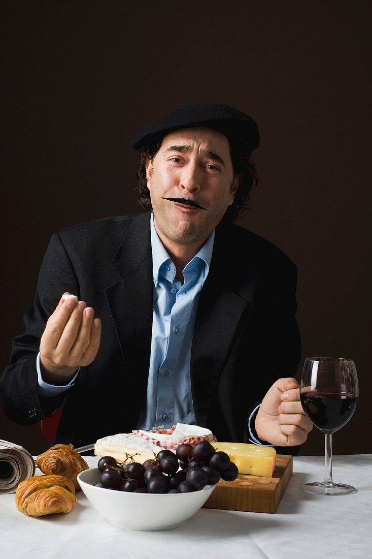 A stereotypical French man eating cheese and grapes