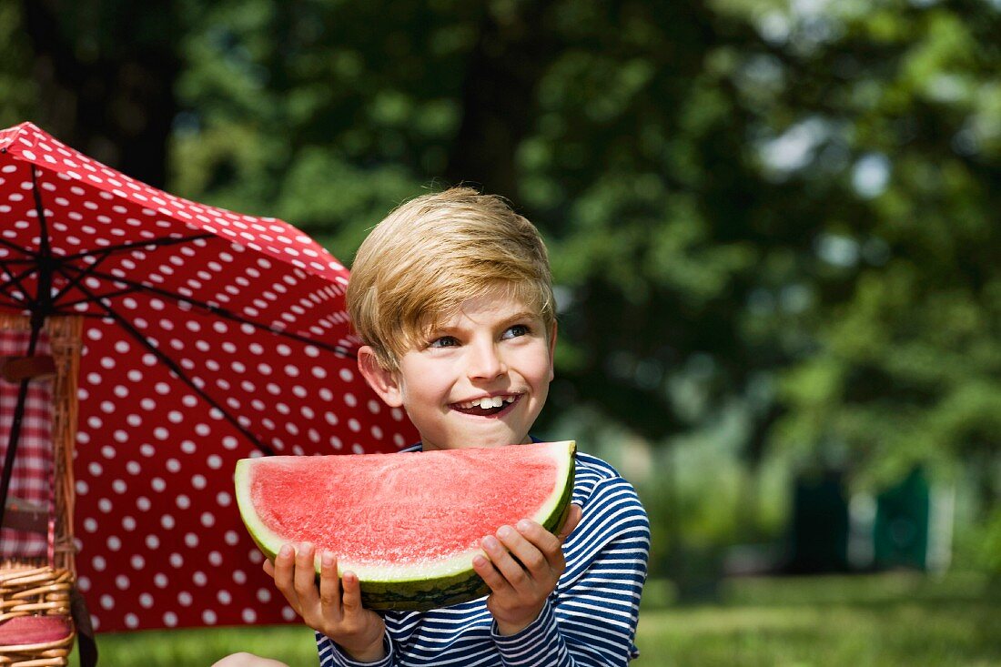 A young boy holding a slice of watermelon at a picnic