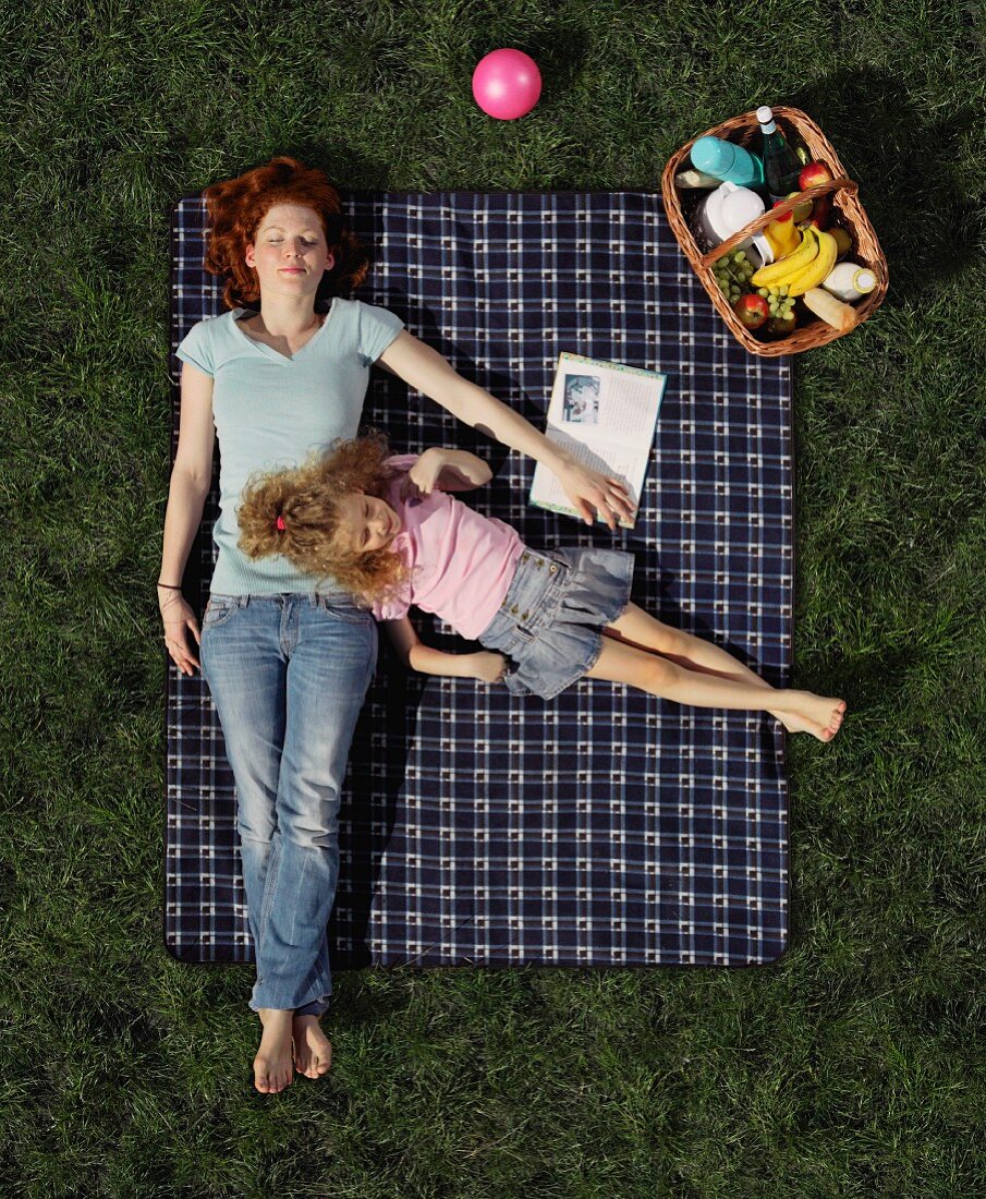 A mother and daughter lying on a picnic blanket on the lawn