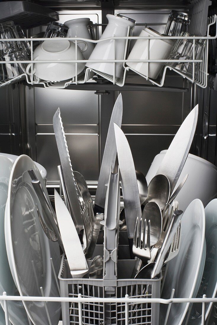 Knives in a dishwasher with the blades pointing dangerously upwards