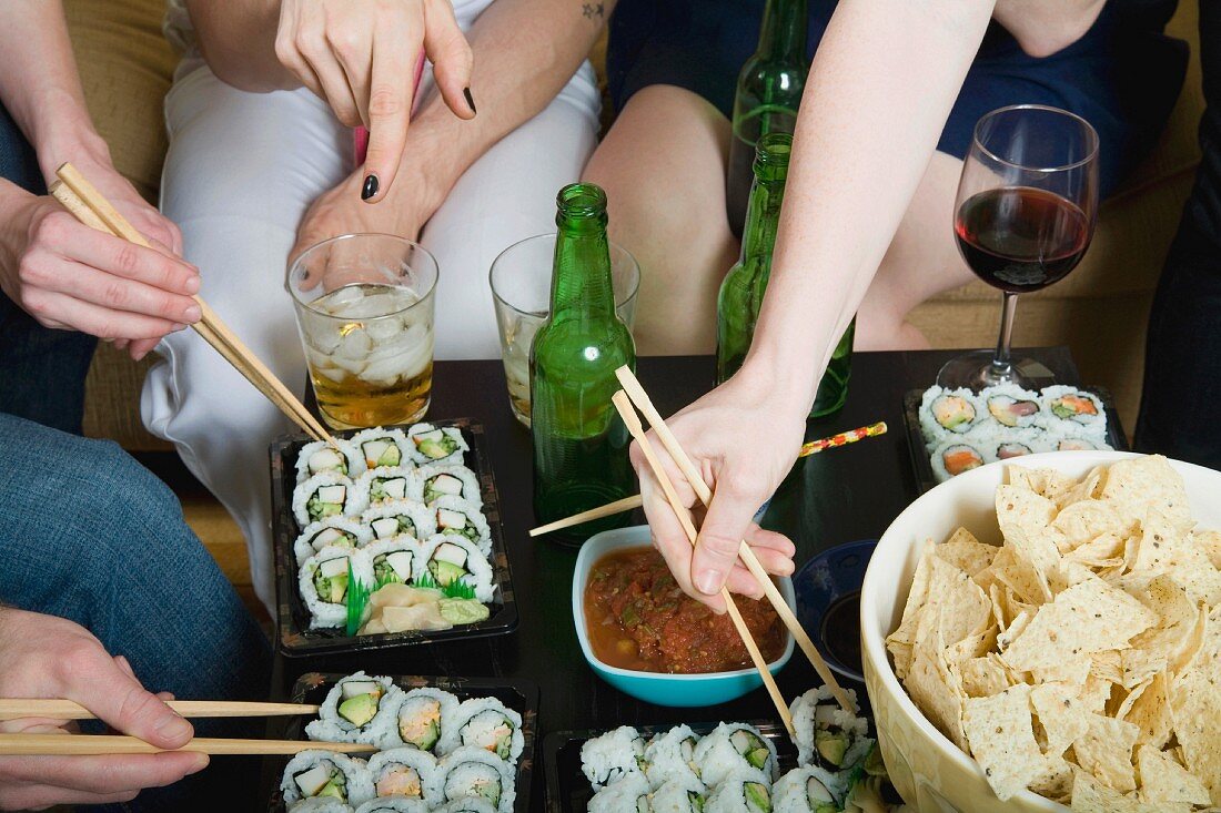 Freunde essen Sushi, Tortillachips und Salsa bei einer Party