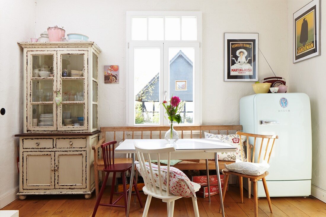 Dining area in rustic ambiance with chairs and bench below window between dresser with glass-fronted top cabinet and fridge