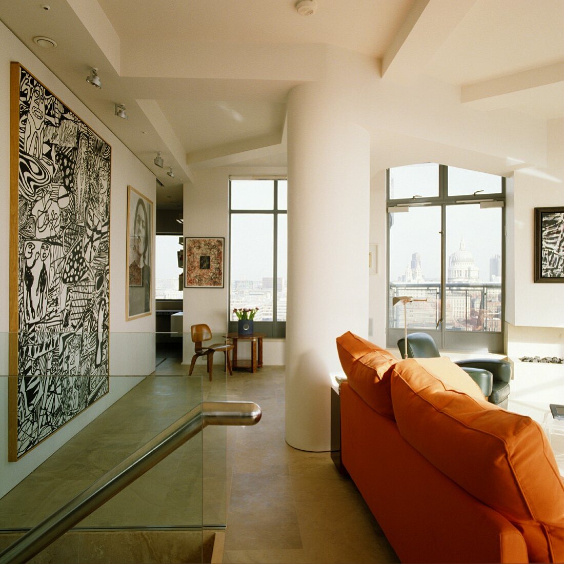 Sofa with orange upholstery in front of modern artwork on wall in living room of penthouse apartment with floor-to-ceiling windows
