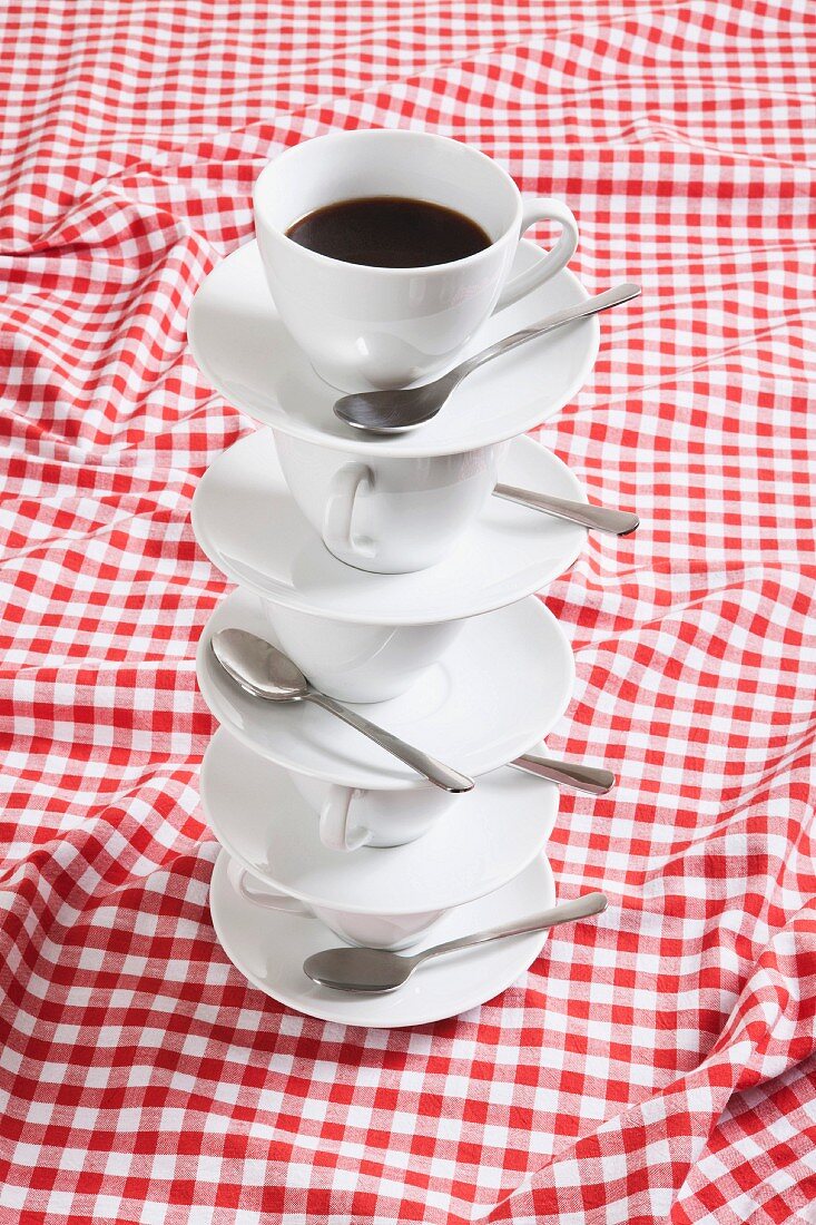 A stack of coffee cups and saucers on a checked tablecloth