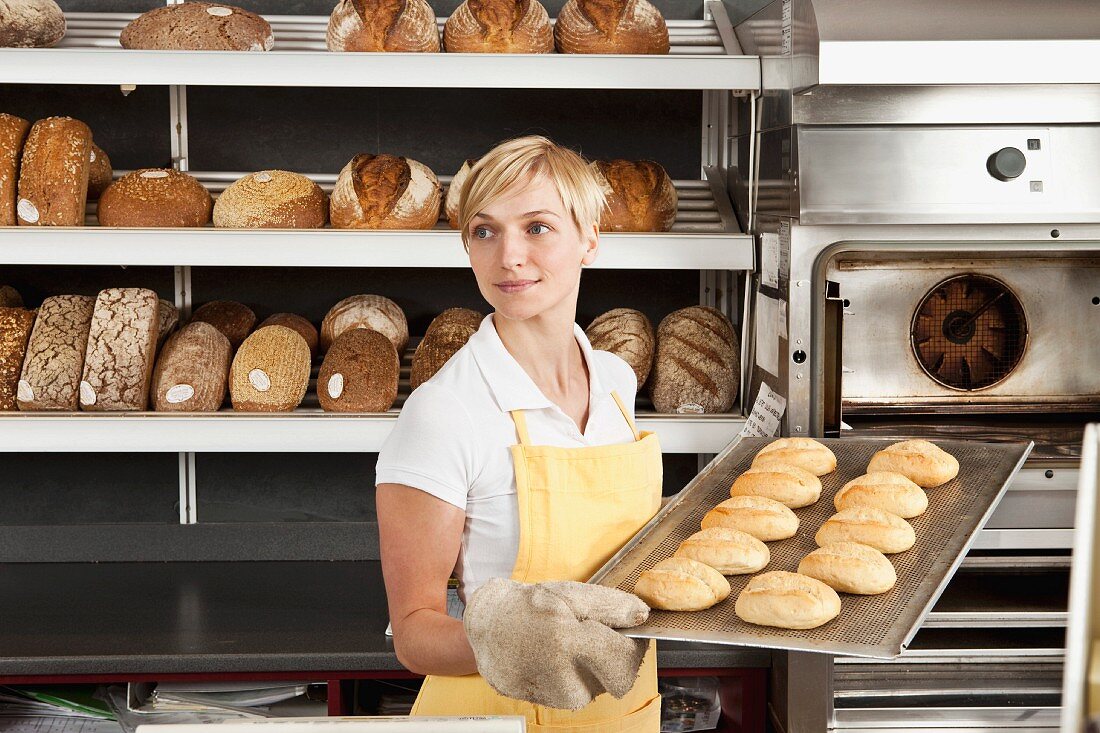 Frau halt Backblech mit frisch gebackenen Brötchen in einer Bäckerei