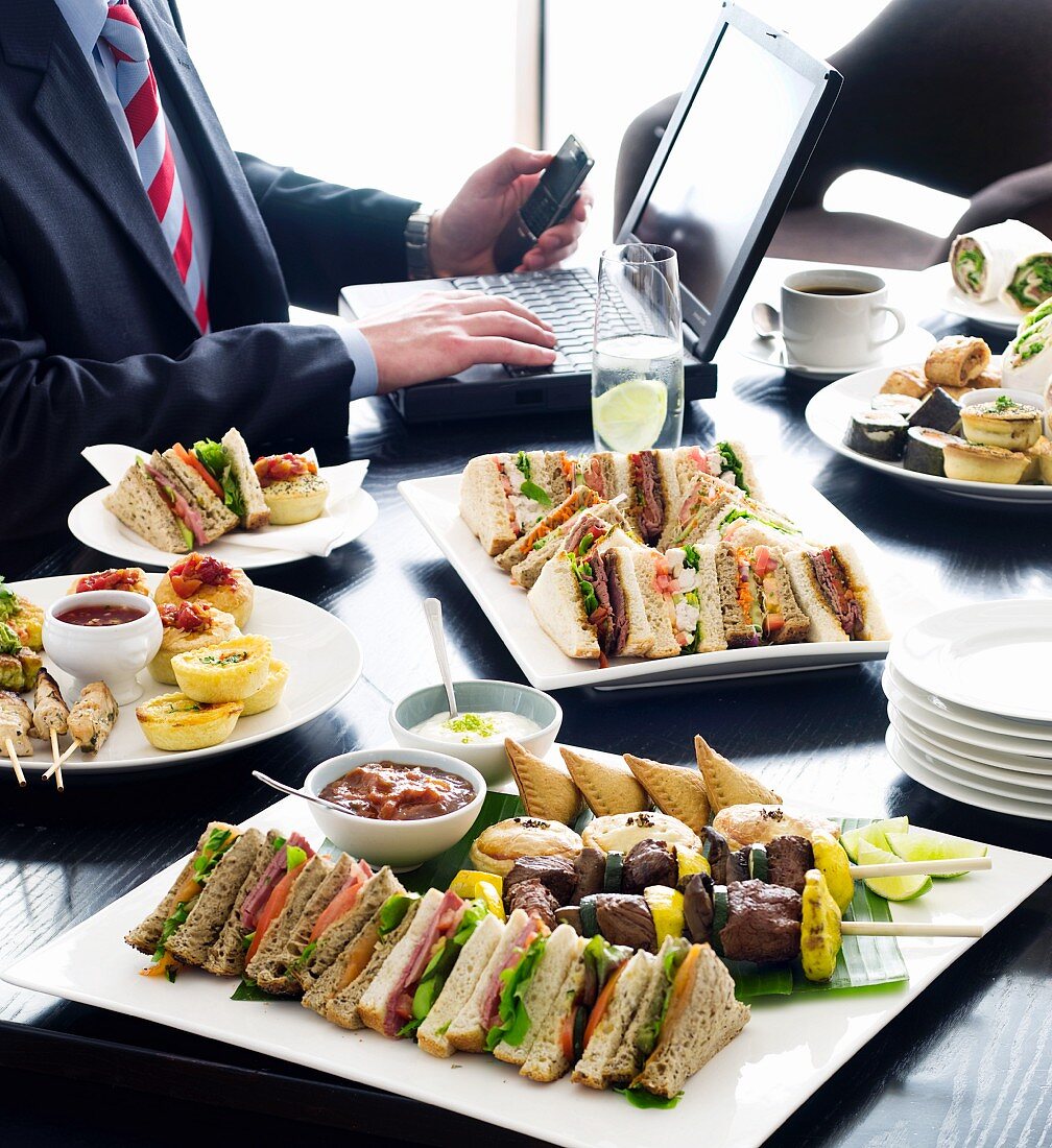 A buffet in a meeting room featuring sandwiches and skewers