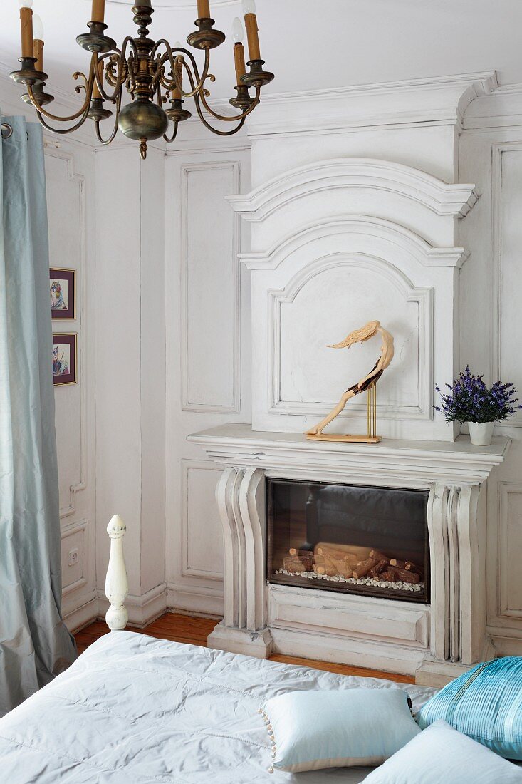 View across bed to fireplace with white, custom fire surround and vintage chandelier