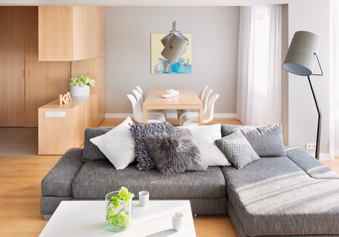 Grey sofa combination with scatter cushions and floodlight standard lamp in open-plan interior with dining area in background