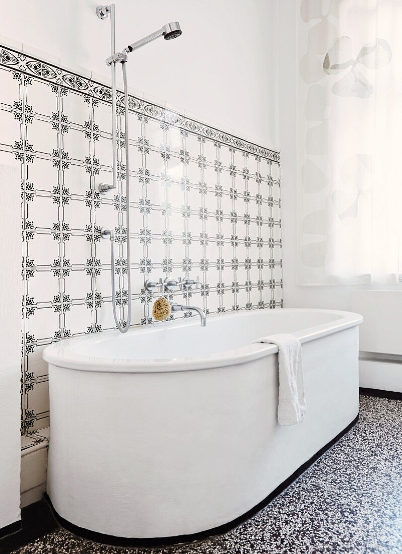 weiße, freistehende Badewanne auf Terrazzoboden, an Wand Fliesen mit schwarz-weißem Vintage Muster