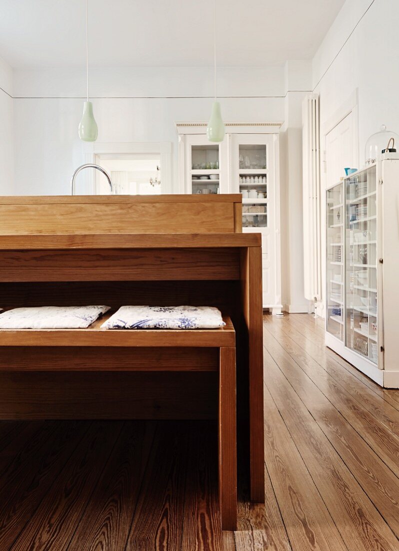 Wooden table and bench set in spacious kitchen with traditional, white-painted cabinets and modern wooden floor with character