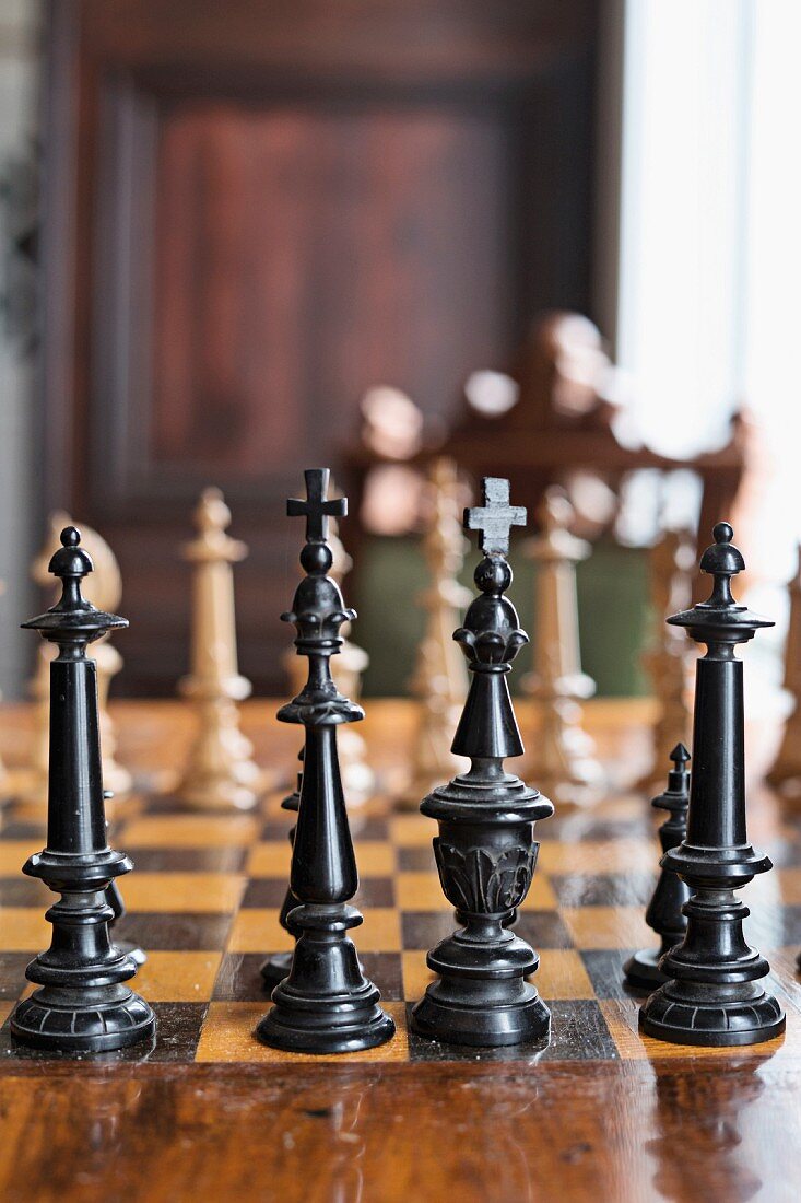 Old chess pieces made from carved, black-painted wood on chessboard