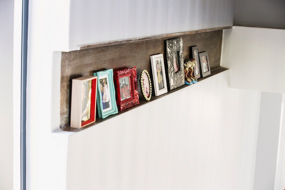 Framed pictures on narrow shelf formed by recess in wall