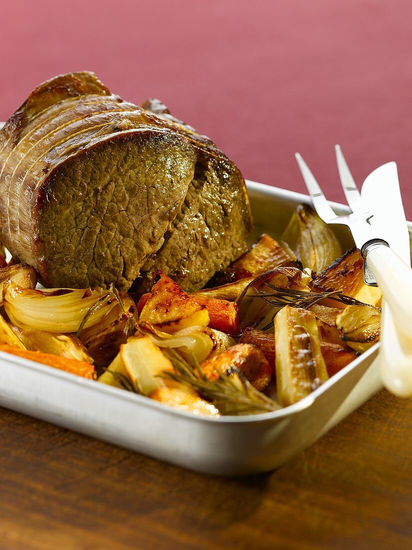 Roast beef with onions and vegetables in a roasting tin
