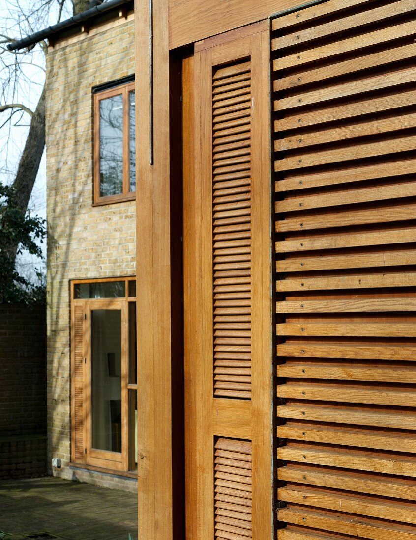 Fensterlade aus hellen Holzlamellen an Wohnhausfassade