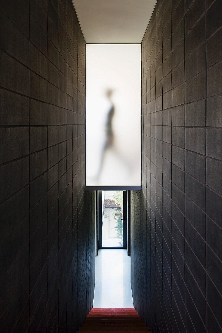 Narrow staircase with black tiled walls and a view down the stairs of a entry way