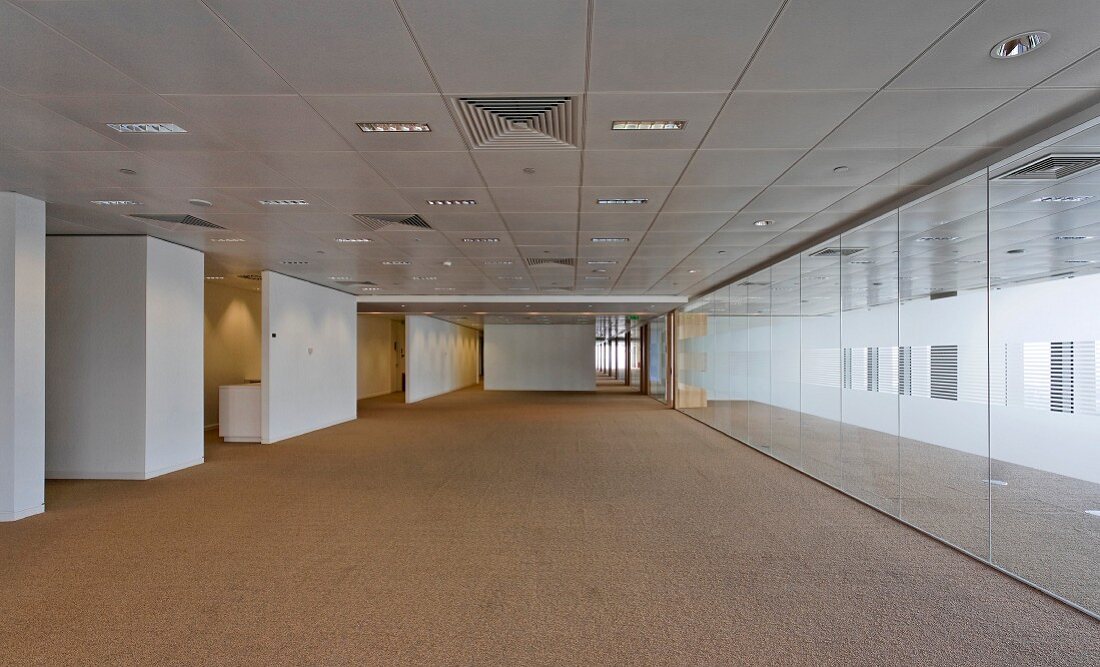 Reflective wall opposite white wall elements in wide corridor with coffer-style ceiling panels