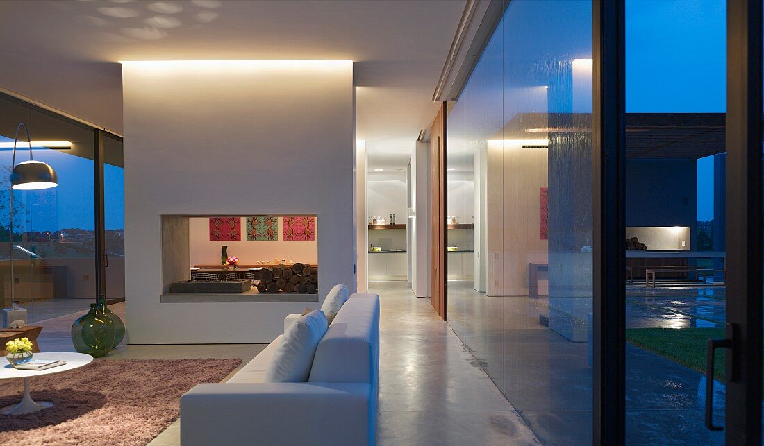 Twilight in living area of glass-walled, South American residence with view of adjacent dining area through wall element