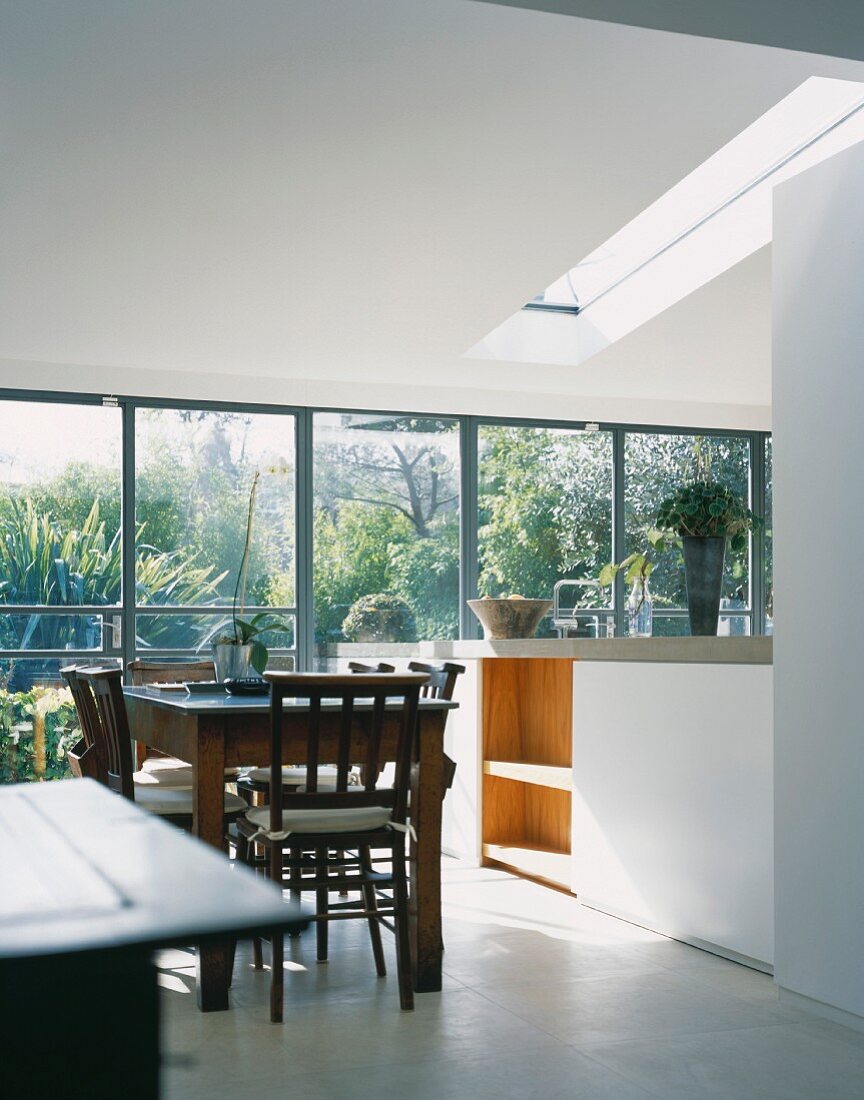 Dining table with chairs made of dark wood in a open-plan, modern kitchen with large bank of windows