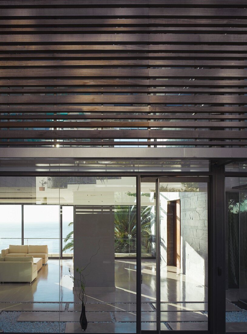 Modern facade of a new building with metal louvres and glassed in first floor with a view of a minimalist living room