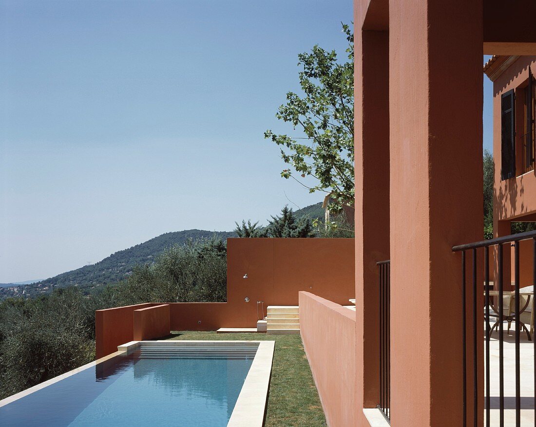 Sun above a pool in a garden and Mediterranean home with a reddish brown facade