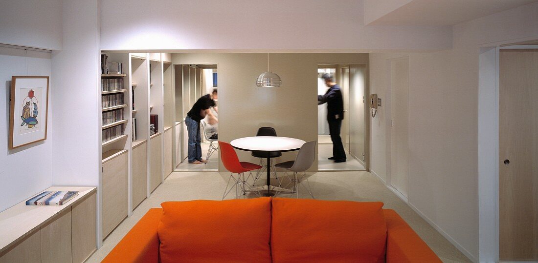 Oranges Sofa und Bistrotisch mit Stühlen aus Bauhauszeit zwischen offenen Durchgängen