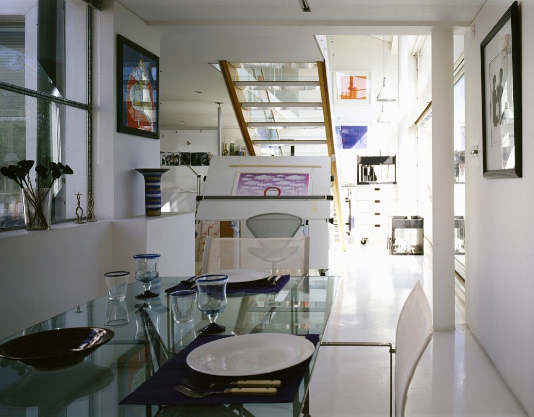Tableware on a glass top dining table in an open, modern living room with stairs