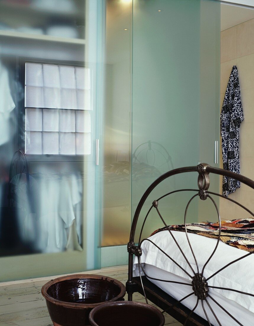 Antique metal bed stead and ceramic pots at the end of the bed in front of the sliding glass doors of the bathroom ensuite