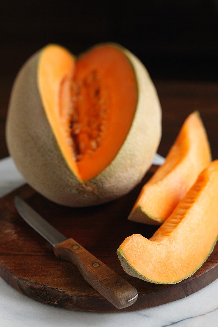 Cantaloupe with Two Wedges Cut Out; On Cutting Board with Knife