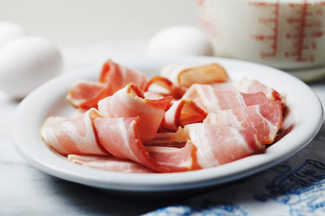 Bacon auf einem Teller mit Eiern und Milch im Hintergrund