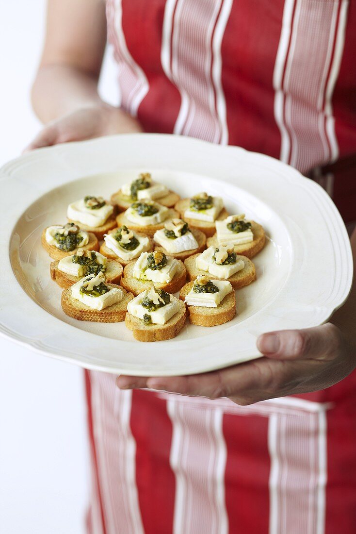 Frau serviert Brothäppchen mit Käse & Pesto