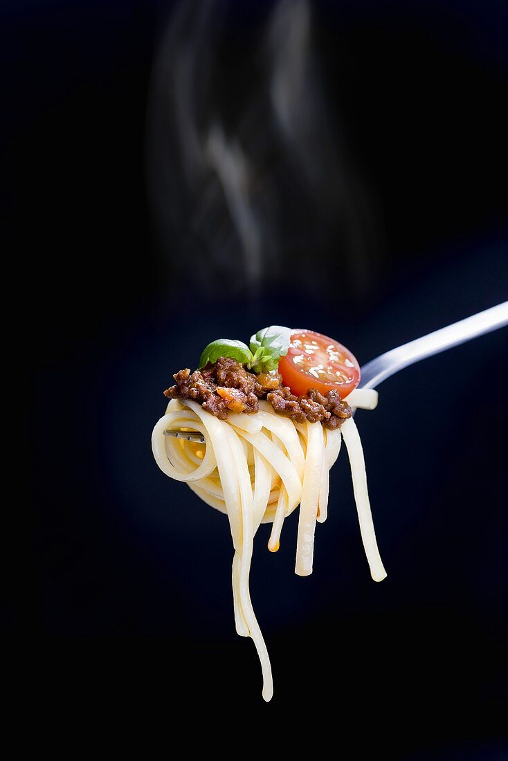 Linguine with a minced meat sauce, tomatoes and basil on a fork