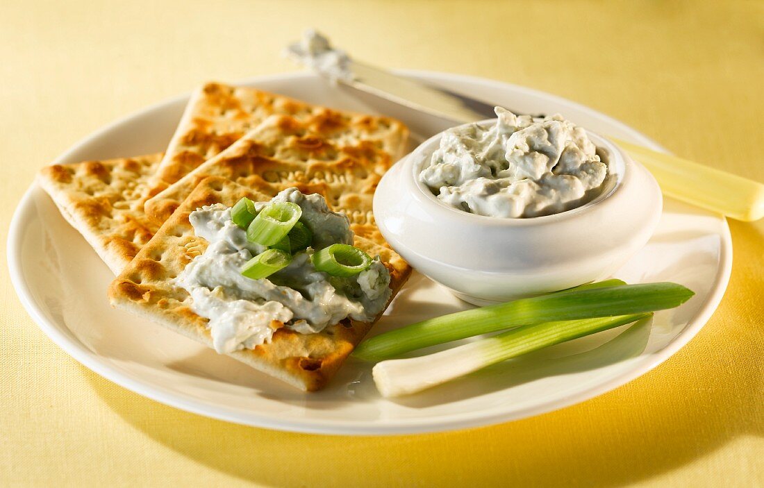 A blue cheese dip with crackers and spring onions