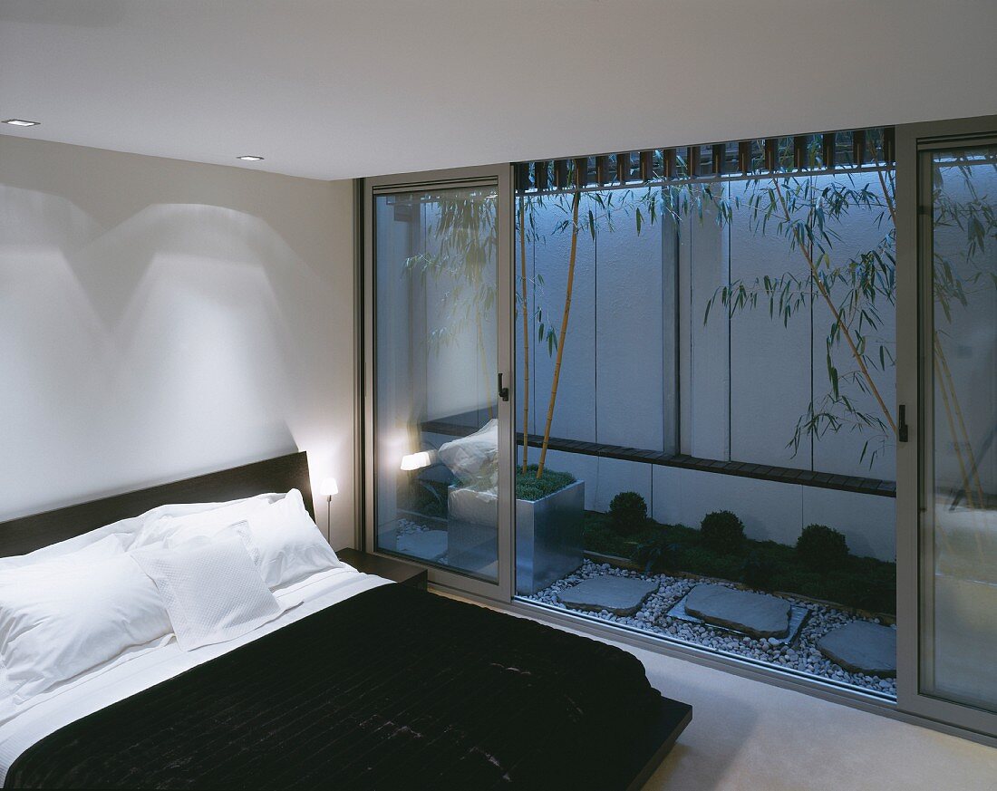 Modern bedroom with a double bed in front of an open, beautifully designed terrace at dusk