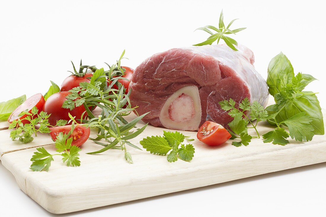 Veal knuckle with herbs and tomatoes on a chopping board