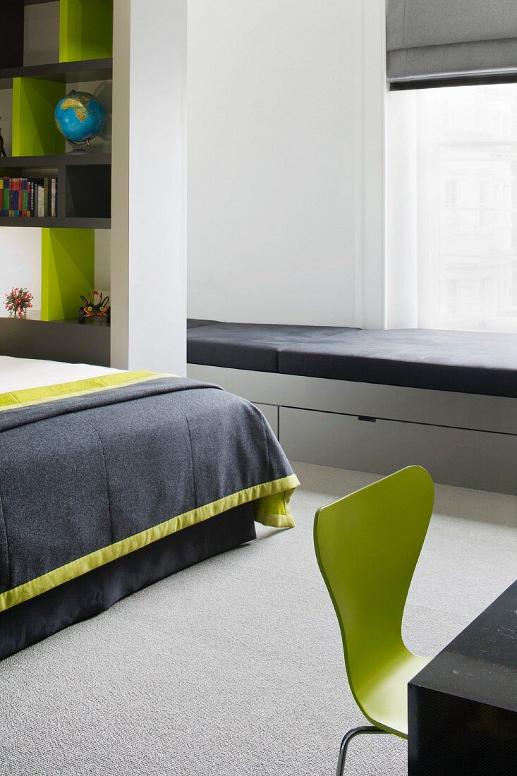 Light gray lacquered window seat upholstered in black and drawers in a modern bedroom with green retro chair