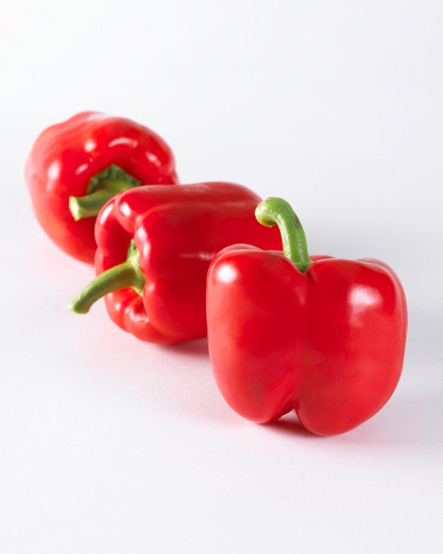 Three red peppers on a white surface