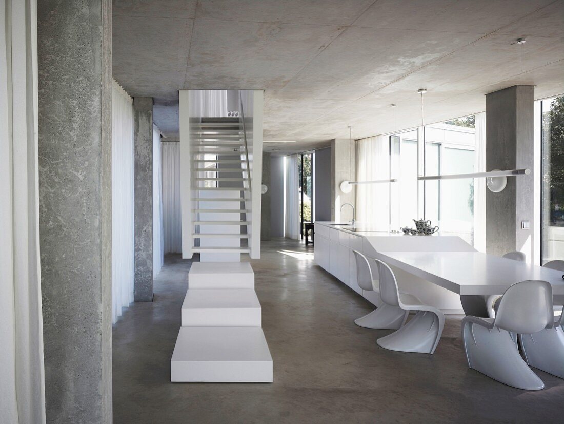 White stair landing in front of stairs in an open living room with shell chairs (in Bauhaus style) in front of a dining table