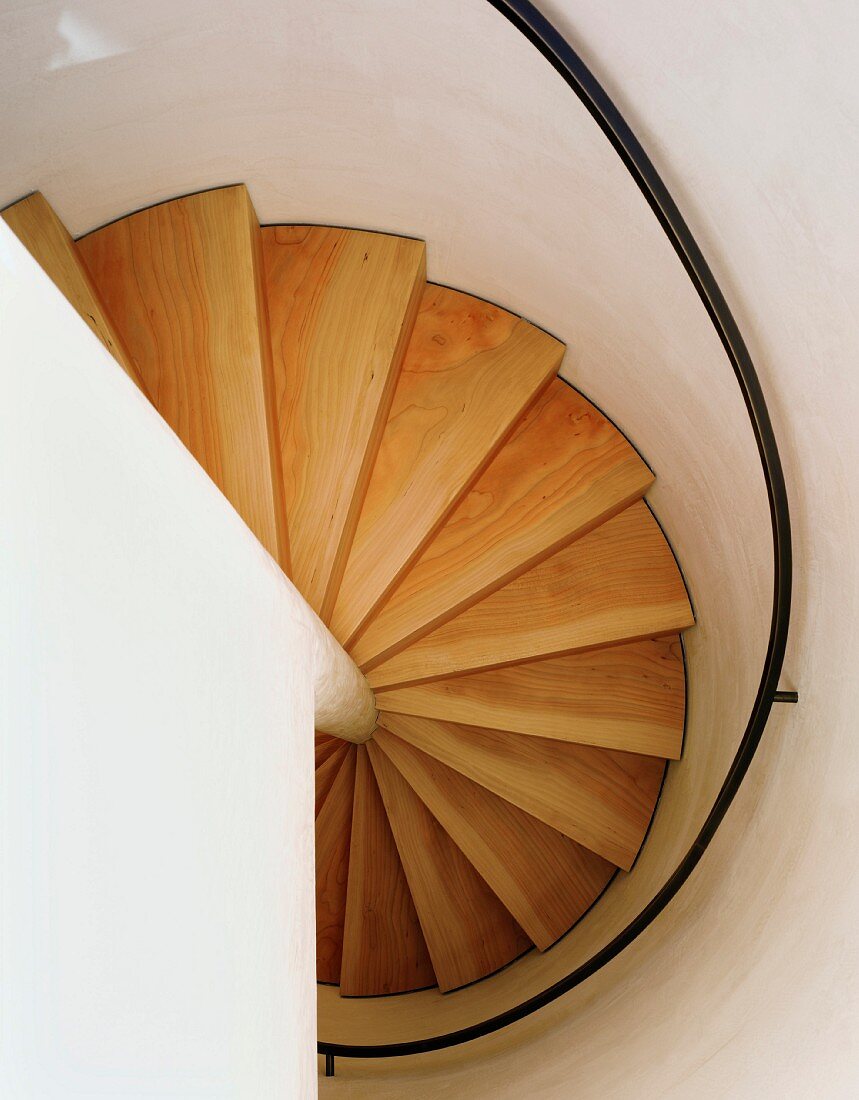 View of a curved stairway with wooden steps and black hand rail in an enclosed stairwll