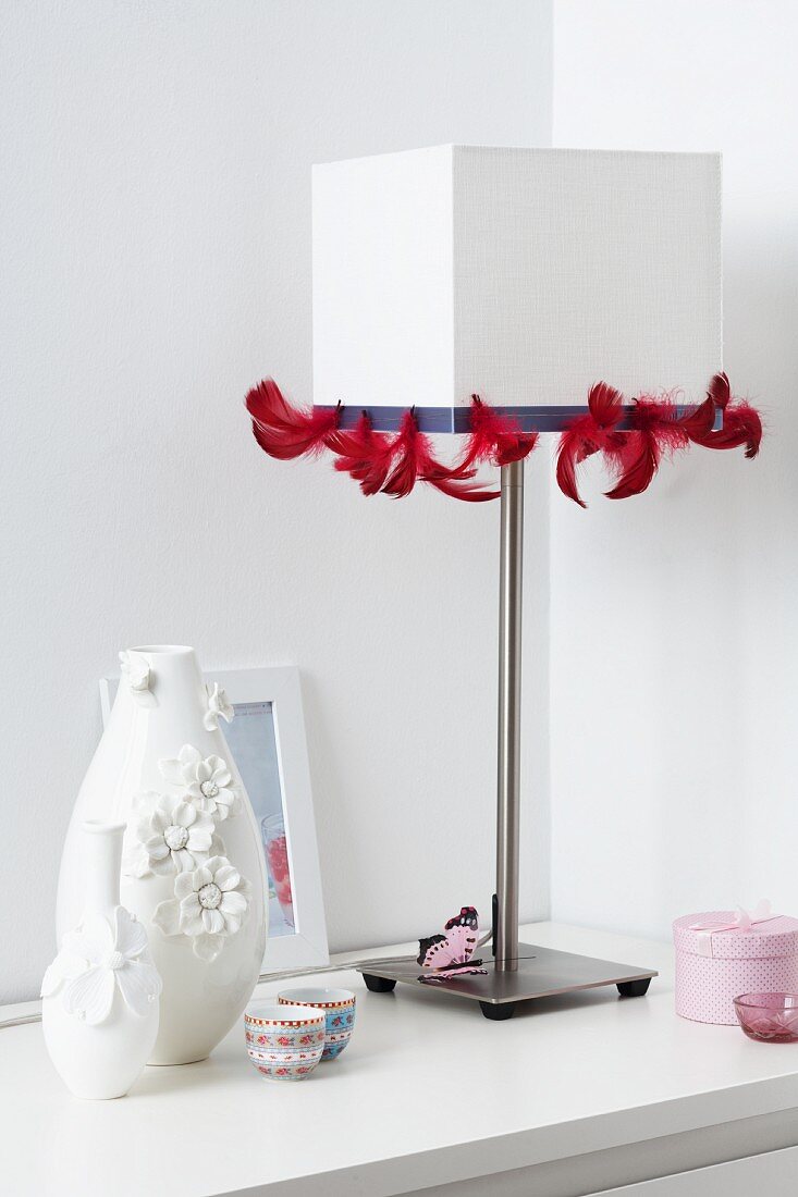 weiße Tischleuchte mit rotem Federband verziert und Vasen mit Blütenapplikation